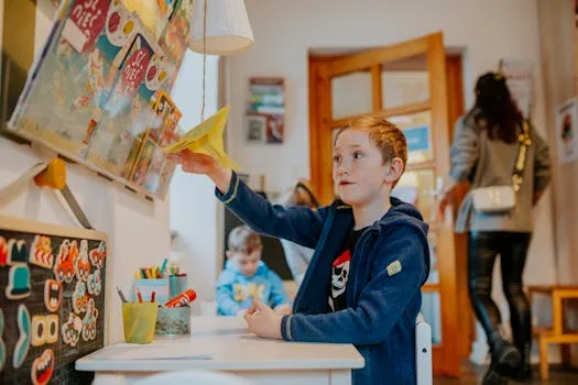 A young boy enjoying a creative activity with a paper airplane in a lively classroom setting.